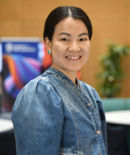 A woman with tanned skin, black hair tied back, brown eyes wearing a blue denim blouse smiling to the camera.